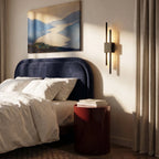 Beside a navy velvet headboard, this matte black Clérachic wall sconce lights a bedside wall with a warm vertical glow.