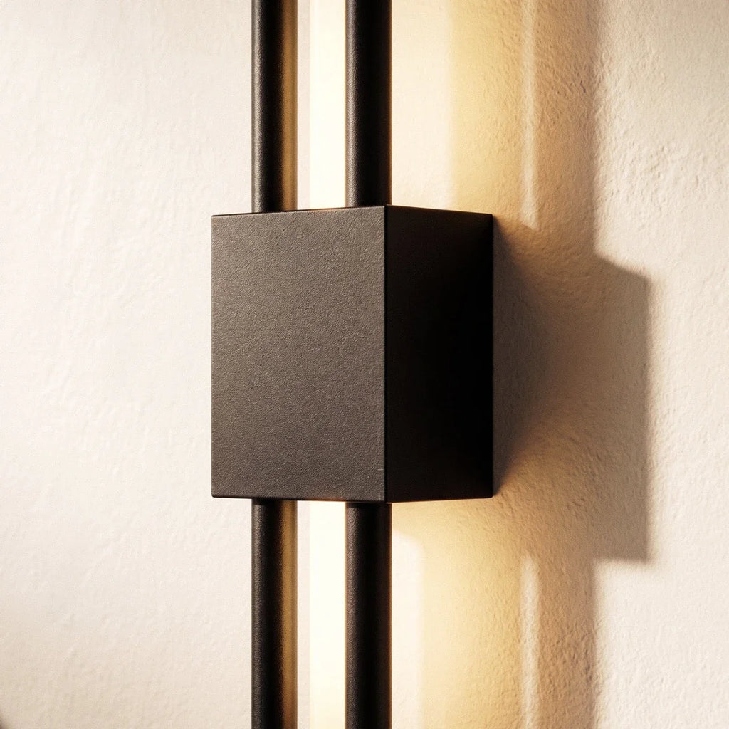An extreme close-up of the Clérachic wall sconce's black square backplate, where two rods cross the lit acrylic strip.