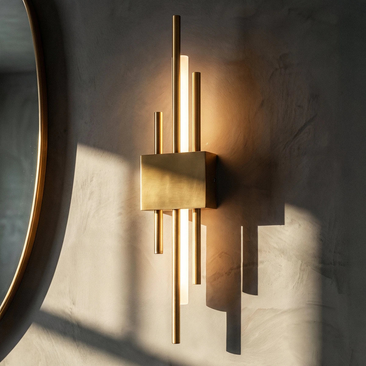 Beside a round brass-framed mirror, this gold Clérachic wall sconce glows warmly against a softly textured wall.