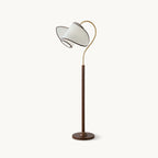 A Clérachic floor lamp with a walnut-colour stem and round base, a brass arc and a white fabric shade, on a plain white backdrop.