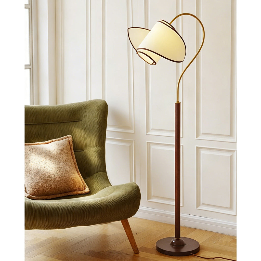 A Clérachic floor lamp stands behind a green armchair with a tan cushion, against white panelling and a parquet floor.