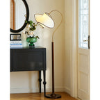 A Clérachic floor lamp stands near a black cabinet and a white door with a glazed panel, its shade arching over the cabinet.