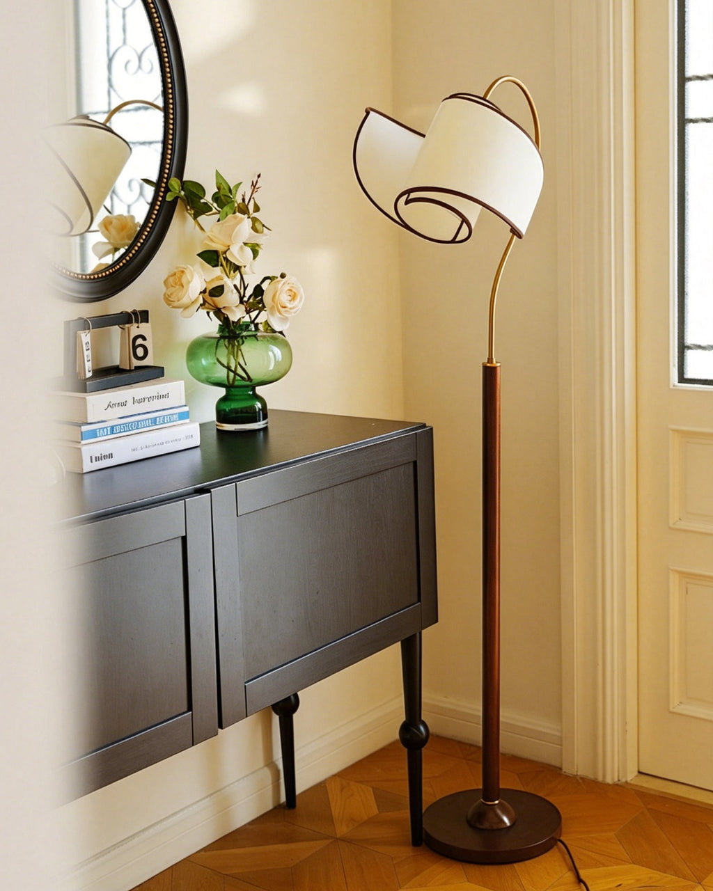 Next to a console with books, a flower vase and a round mirror, a Clérachic floor lamp with a wood-colour stem.