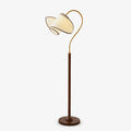 A Clérachic floor lamp with a dark wood-colour stem, a brass arc and a folded white shade, on a pale grey backdrop.
