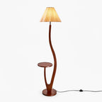 Curved dark-wood floor lamp with a round tray table partway down the stem and a pleated cream shade, shown on white for this Clérachic lamp.