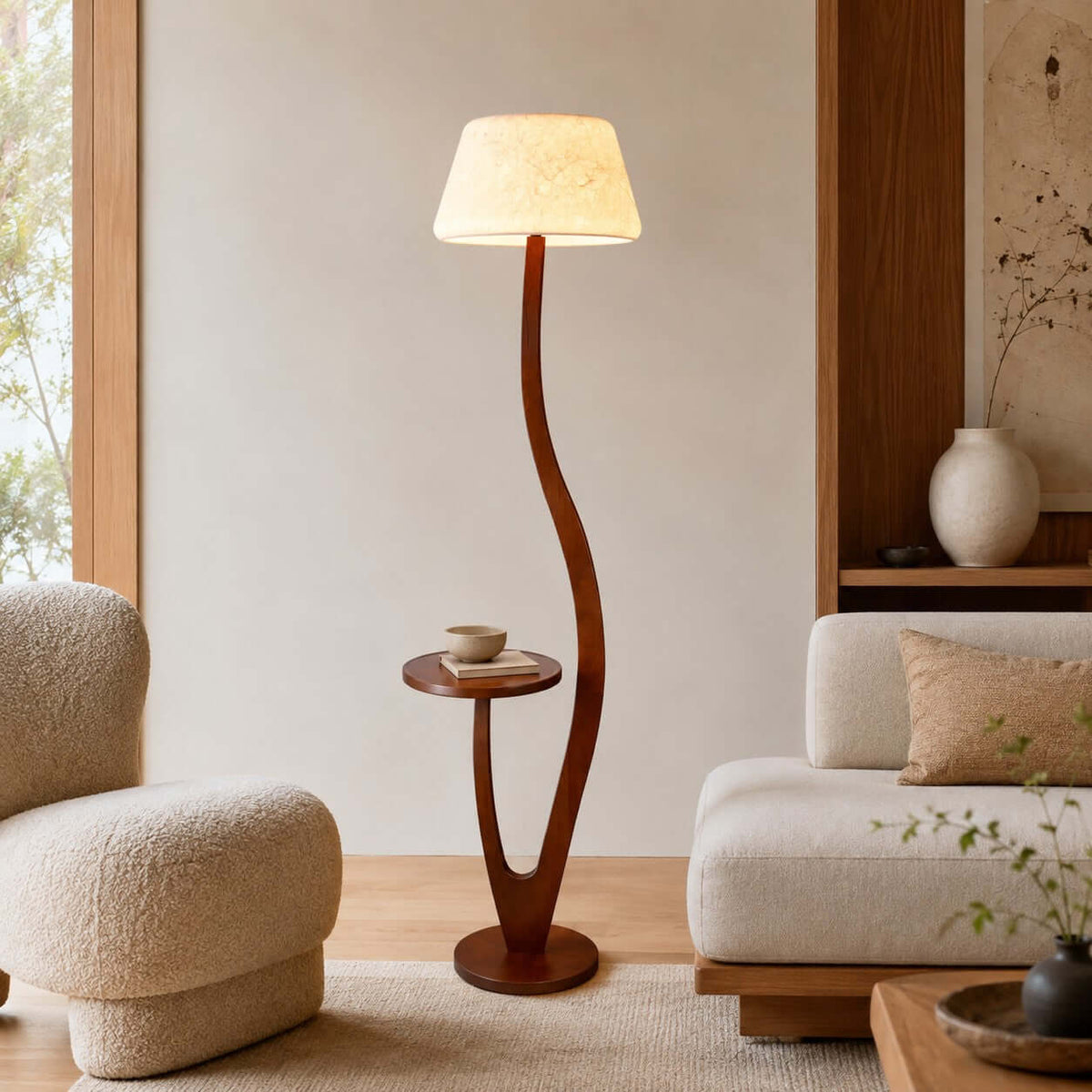 A cream drum-style shade sits on a sweeping curved wooden stem beside a low cream sofa, with a cup resting on this Clérachic lamp's tray.