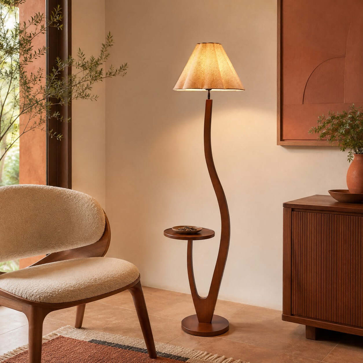 A pleated shade glows warm over a curved wooden stem with a small tray, next to a rounded boucle chair and a ribbed cabinet, from Clérachic.