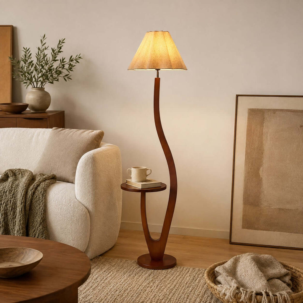 This Clérachic floor lamp stands beside a cream armchair and a framed artwork, a mug and a book resting on its round wooden tray.