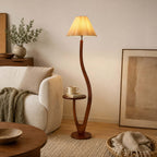 This Clérachic floor lamp stands beside a cream armchair and a framed artwork, a mug and a book resting on its round wooden tray.
