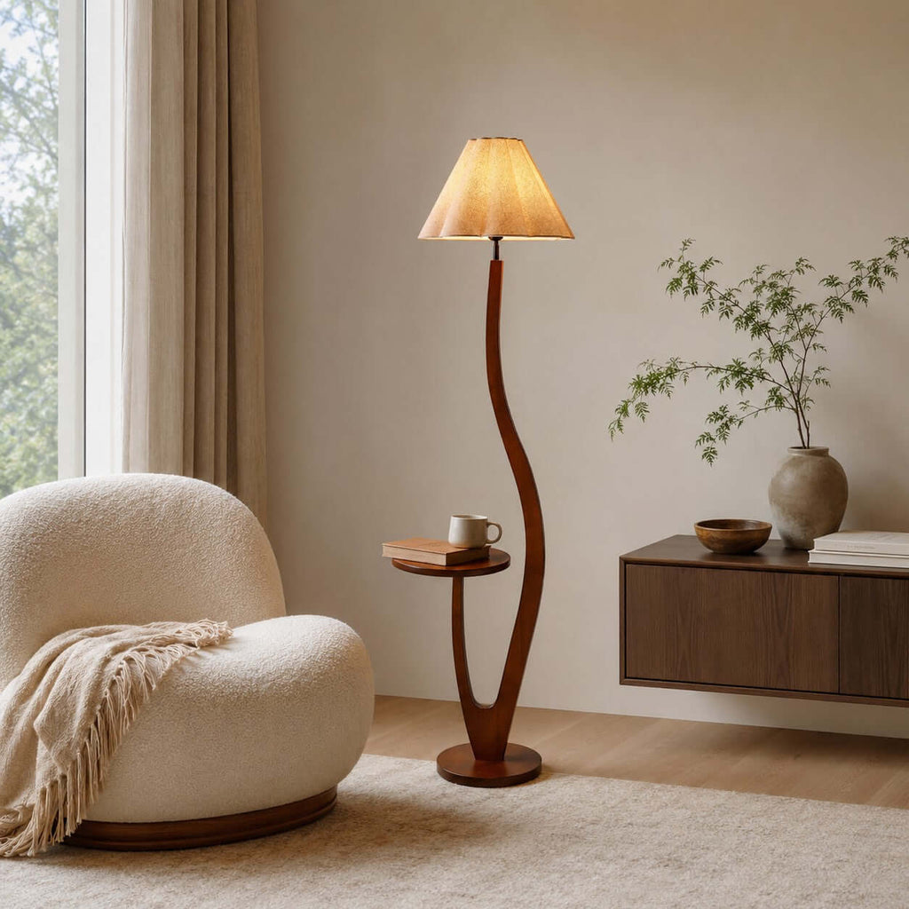A pleated shade lights a corner with a boucle chair and a floating walnut shelf, the lamp's tray holding a cup, from Clérachic.