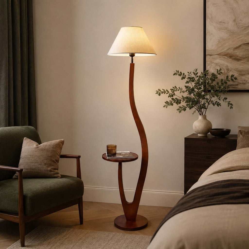 Beside a green armchair and a bed, this Clérachic floor lamp's cream shade glows above a curved wooden stem and a small round tray.