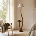 A plain tapered linen shade tops this Clérachic floor lamp, with a bowl on its tray and a wooden chair draped with a green throw beside it.