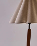Close view of the folded, pleated linen shade and the black fitting on top of the curved wooden stem of this Clérachic floor lamp.