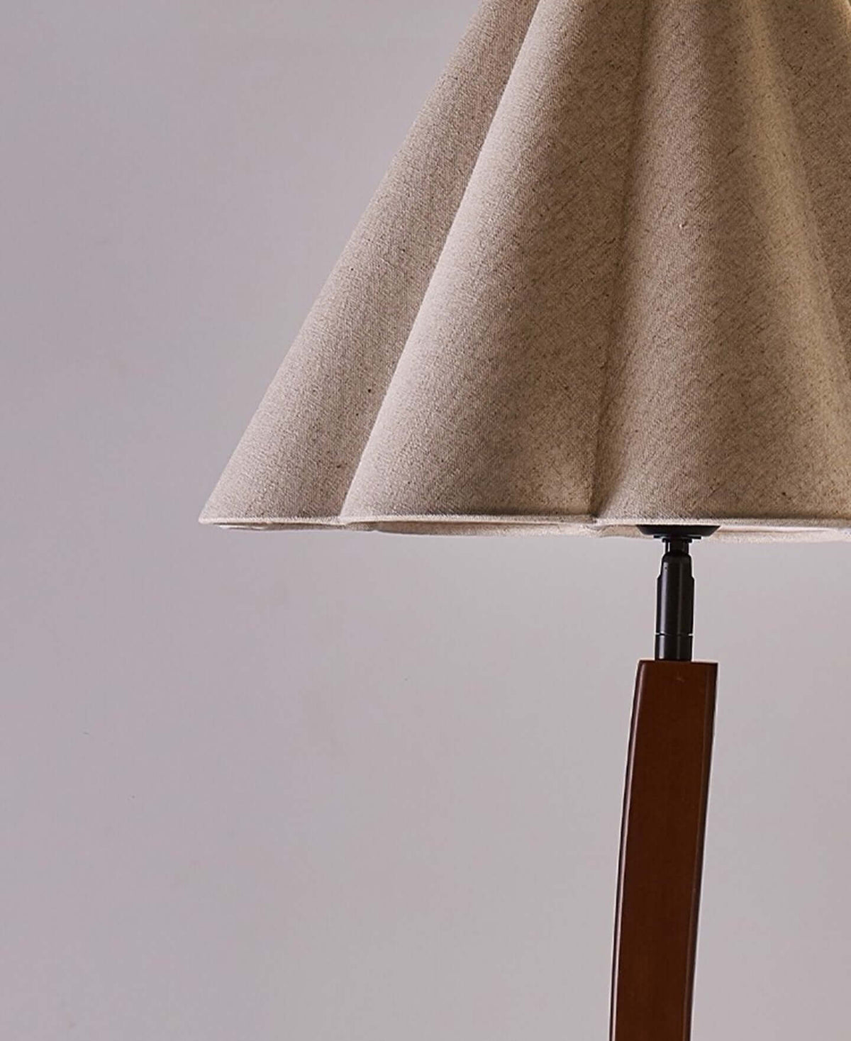 Close view of the folded, pleated linen shade and the black fitting on top of the curved wooden stem of this Clérachic floor lamp.