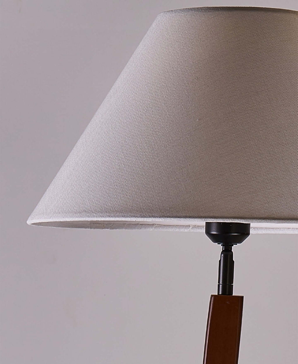 Close view of a plain tapered shade in grey-beige fabric and a slim black fitting above the wooden stem, on this Clérachic floor lamp.