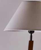 Close view of a plain tapered shade in grey-beige fabric and a slim black fitting above the wooden stem, on this Clérachic floor lamp.