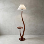 This Clérachic floor lamp with a plain cream tapered shade stands on a pale concrete floor against a grey plaster wall.