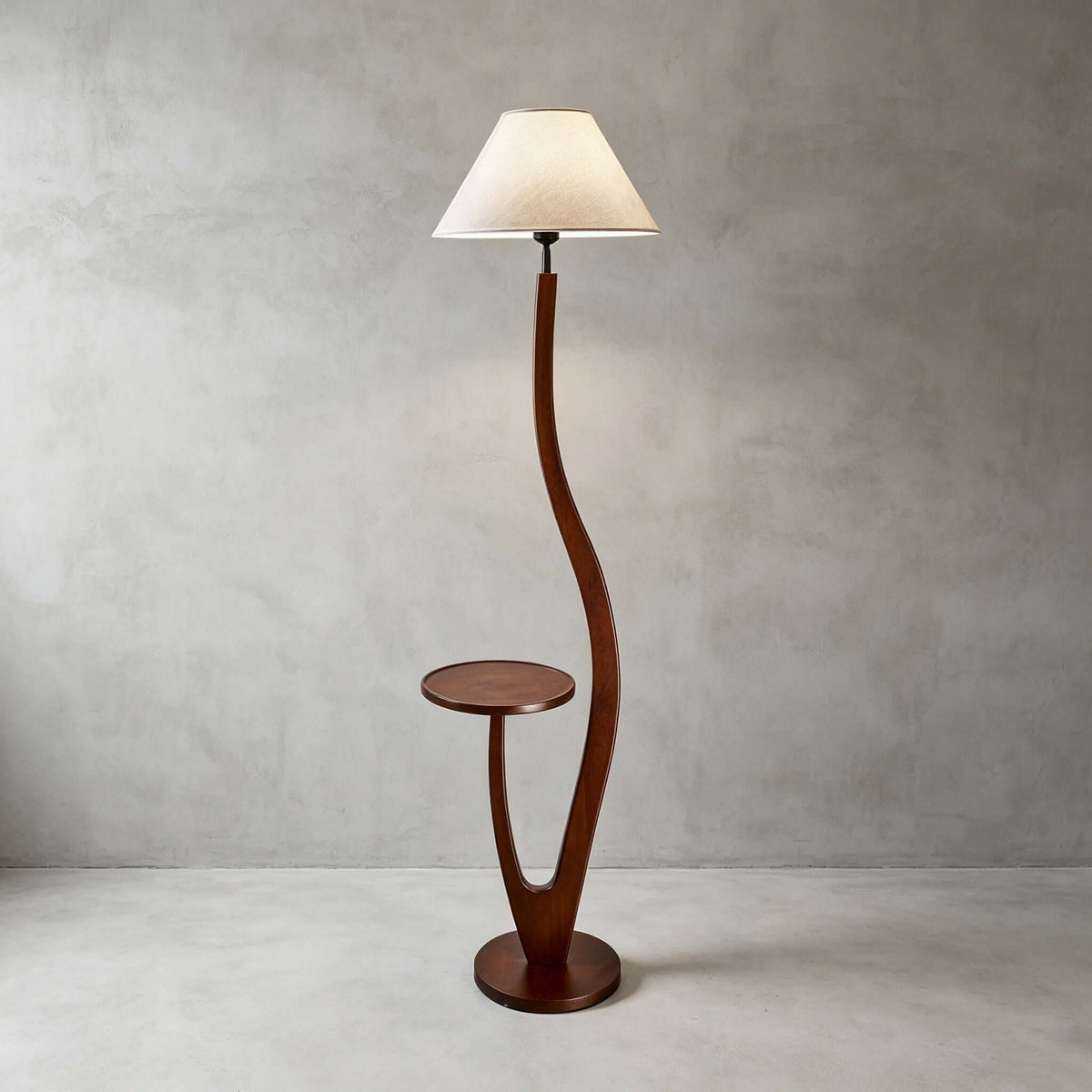 This Clérachic floor lamp with a plain cream tapered shade stands on a pale concrete floor against a grey plaster wall.