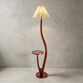 With its pleated shade lit warm, this Clérachic floor lamp stands against a grey plaster wall on a pale floor.