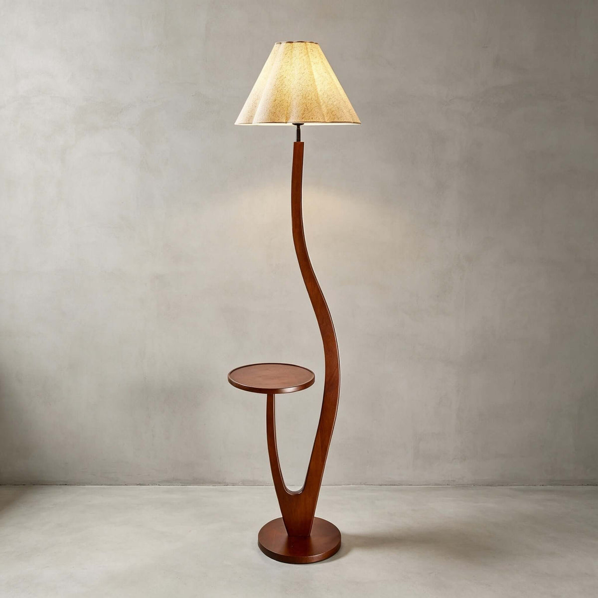 With its pleated shade lit warm, this Clérachic floor lamp stands against a grey plaster wall on a pale floor.