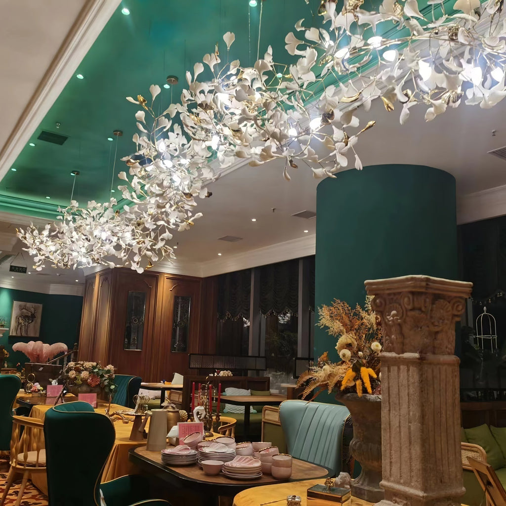 Clérachic gingko chandelier lit across a green restaurant ceiling above set tables.
