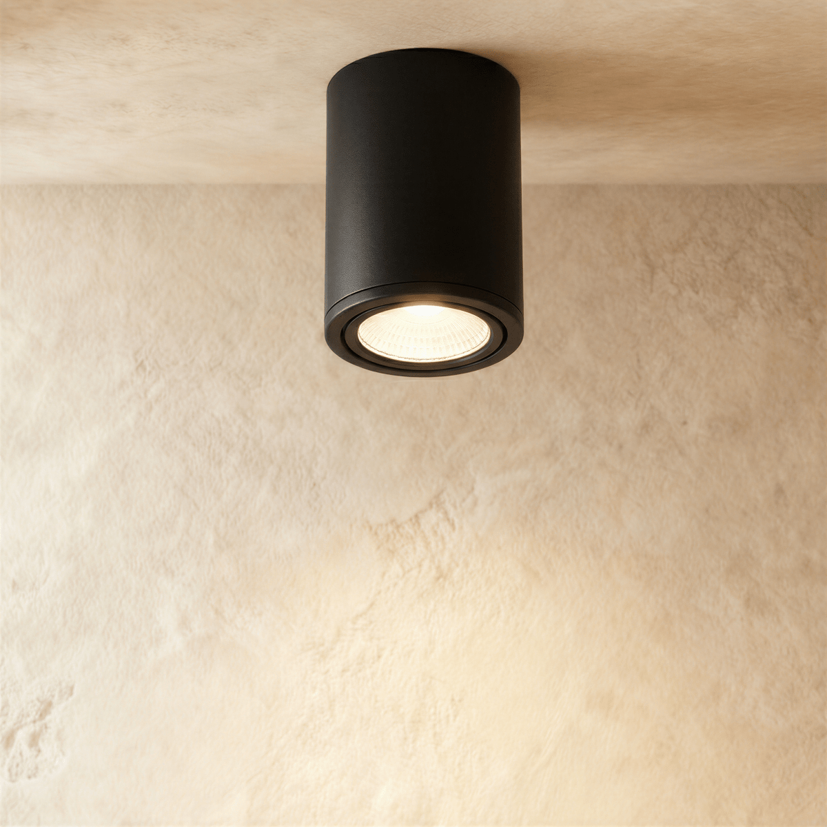 Clérachic black aluminium cylinder downlight, surface-mounted on a limewash ceiling and glowing warm from its recessed lens.