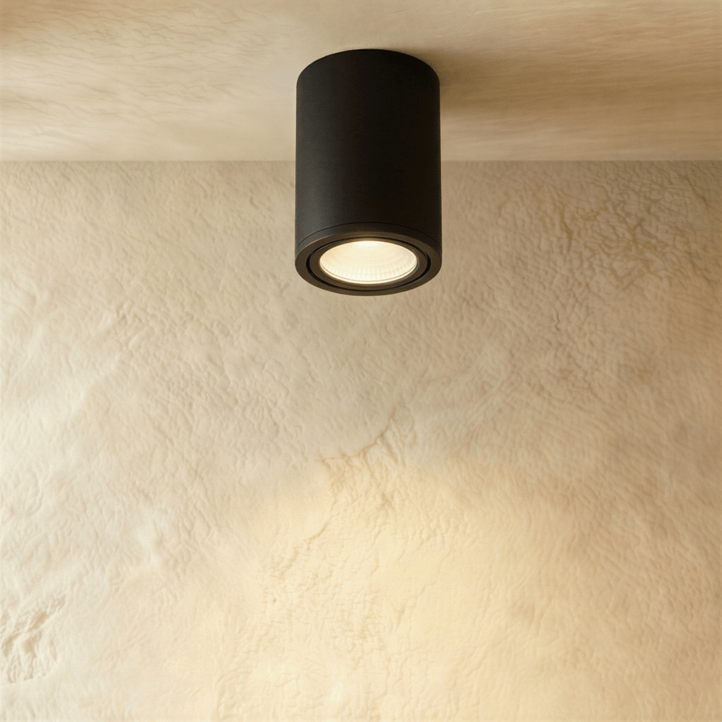 Clérachic compact black aluminium cylinder downlight, lit warm against a plastered ceiling and wall.