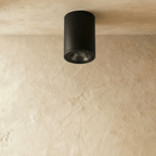 Clérachic compact black cylinder downlight, unlit, with its dark reflector and trim ring visible on a limewash ceiling.