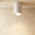 Clérachic white aluminium cylinder downlight, surface-mounted and glowing warm on a limewash ceiling.