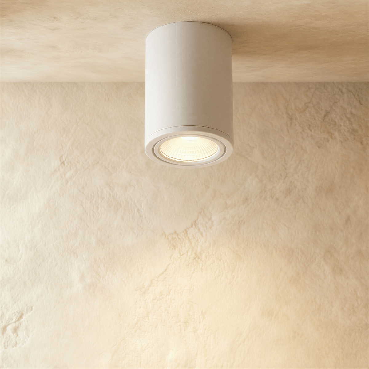 Clérachic white aluminium cylinder downlight, surface-mounted and glowing warm on a limewash ceiling.