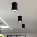 Three Clérachic black cylinder downlights in graduated sizes, lighting a pale ceiling above an open-plan interior.