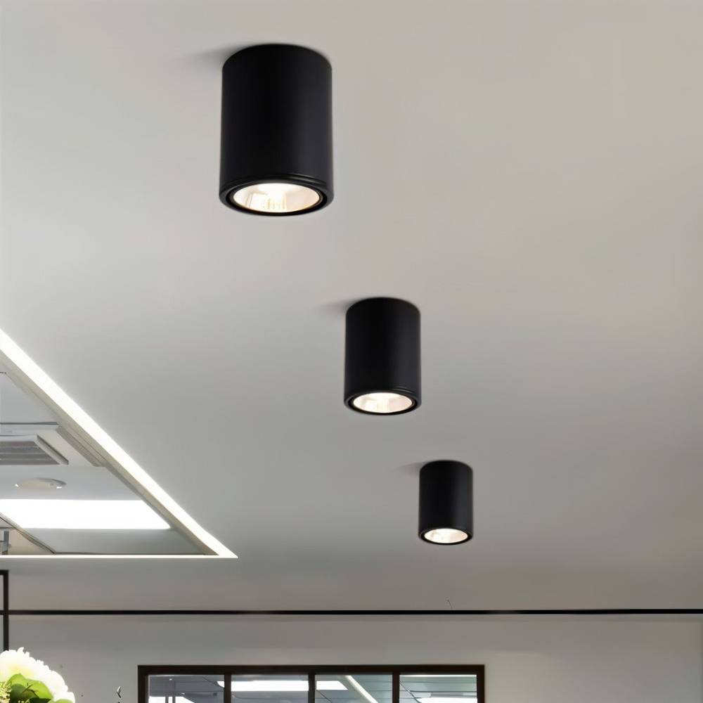 Three Clérachic black cylinder downlights in graduated sizes, lighting a pale ceiling above an open-plan interior.