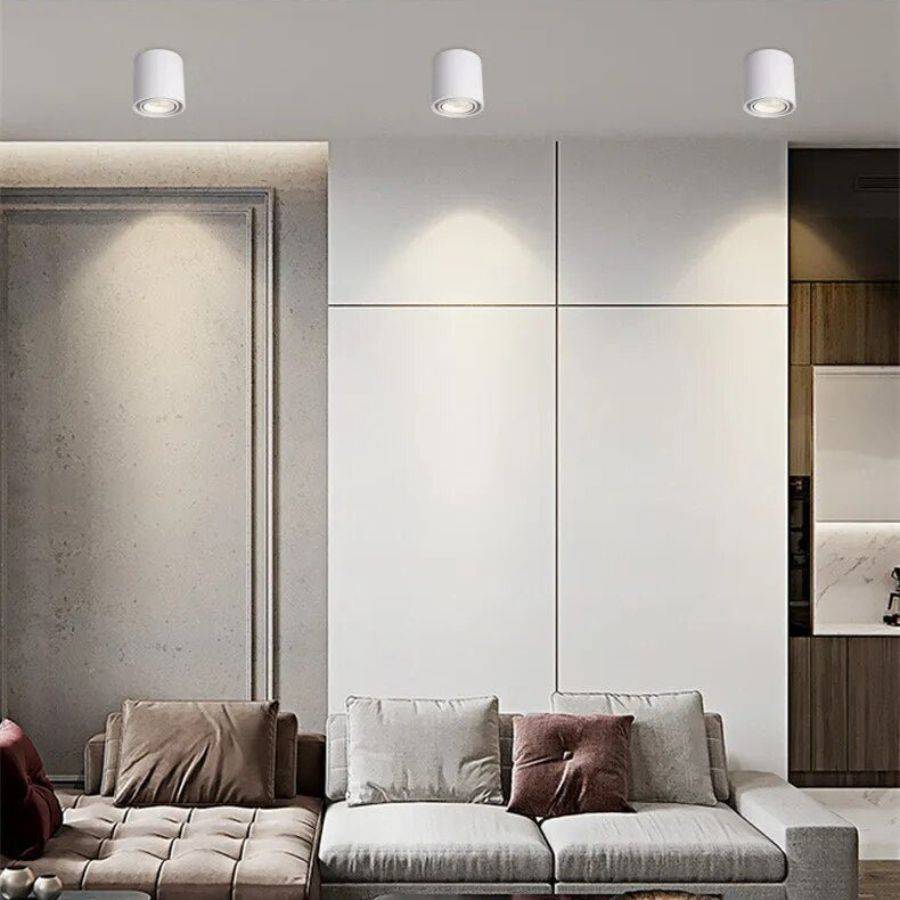 Three Clérachic white cylinder downlights lighting a living room ceiling, washing a panelled wall above a sofa with light.