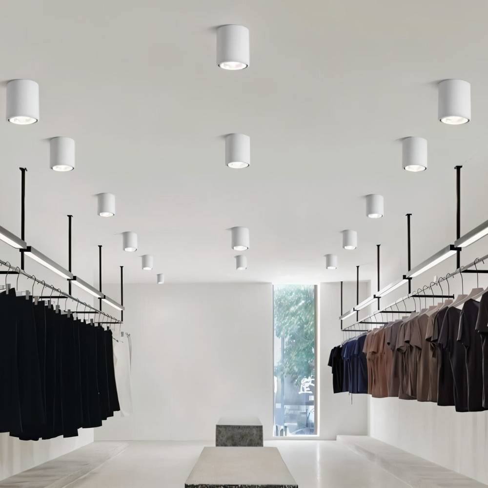 Clérachic white cylinder downlights in graduated sizes, spaced across a high ceiling above a minimal clothing store.