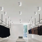 Clérachic white cylinder downlights in graduated sizes, spaced across a high ceiling above a minimal clothing store.