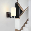 Clérachic black glass cylinder wall sconce mounted beside a staircase with an angled black and brass railing.