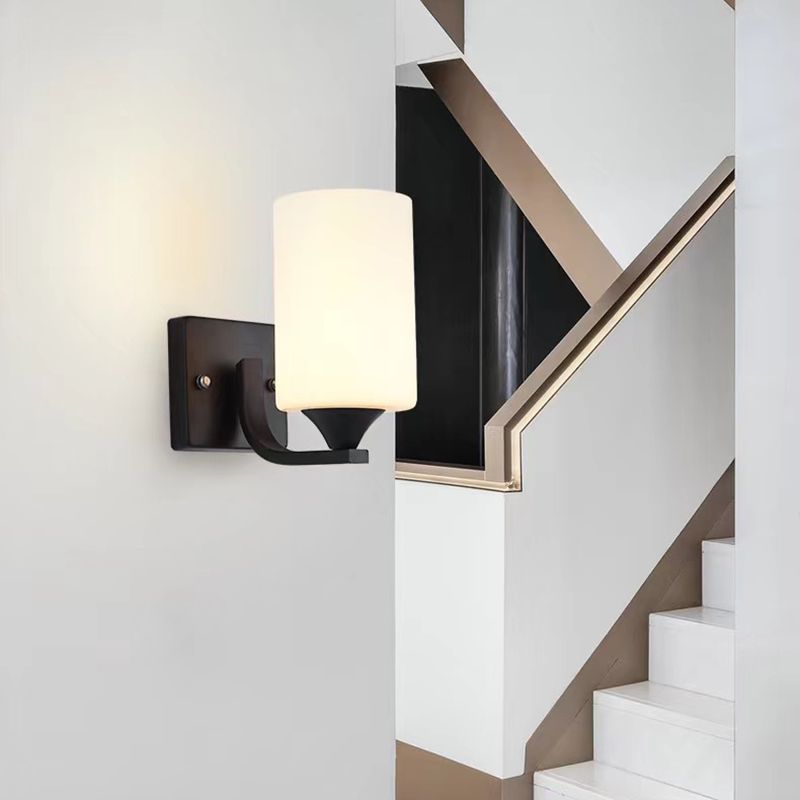 Clérachic black glass cylinder wall sconce mounted beside a staircase with an angled black and brass railing.