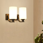 Clérachic black two-light glass cylinder wall sconce mounted on a beige wall beside a potted plant.