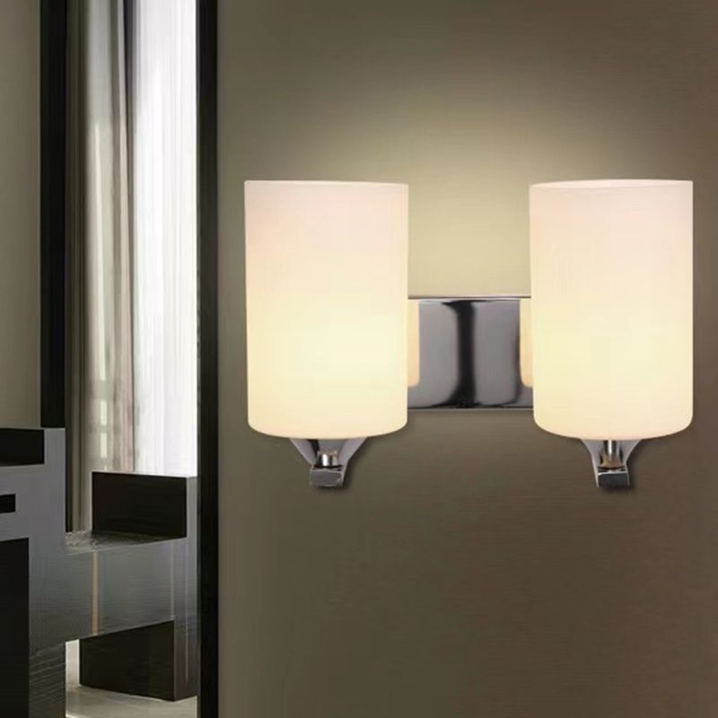 Clérachic polished chrome two-light glass cylinder wall sconce glowing on a dark wall beside a curtained window.