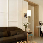 Clérachic black glass cylinder wall sconce lit above a console table with fresh flowers in a living room.