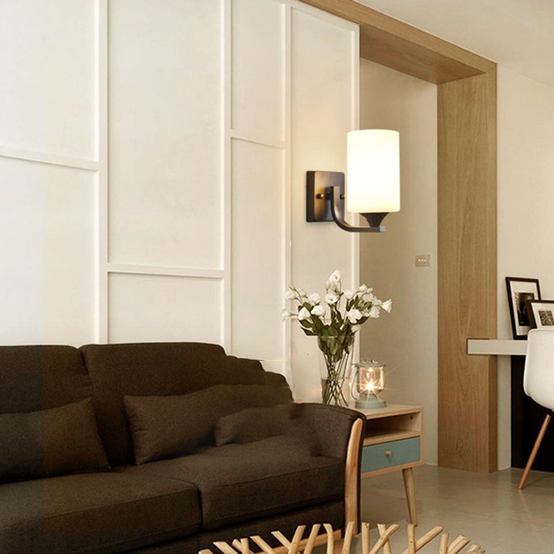 Clérachic black glass cylinder wall sconce lit above a console table with fresh flowers in a living room.