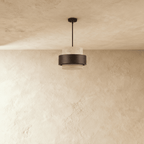 Clérachic travertine drum pendant with a dark wood band, switched off and hung from a black rod over a textured plaster wall.