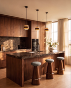 Clérachic three travertine and wood drum pendants glowing warm over a marble-topped walnut kitchen island with grey stools.