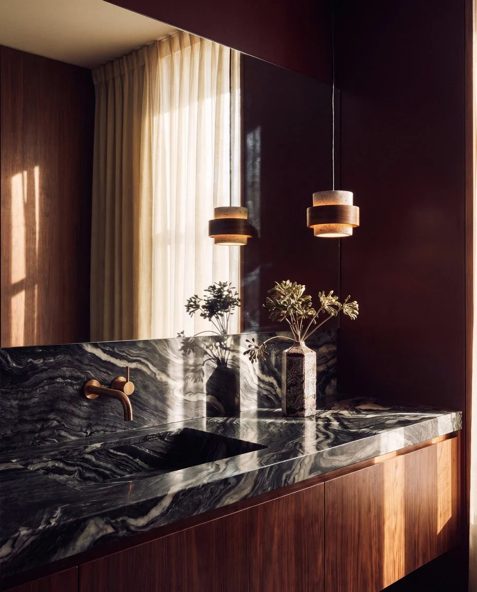 Clérachic small drum pendant of travertine and dark wood, hanging beside a mirror above a marble counter and walnut cabinet.