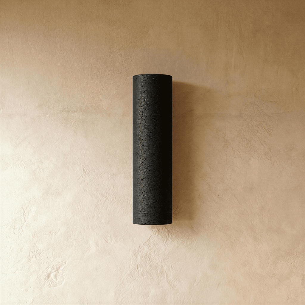 Clérachic black textured stone-look cylinder wall light, mounted upright on a warm limewash plaster wall.