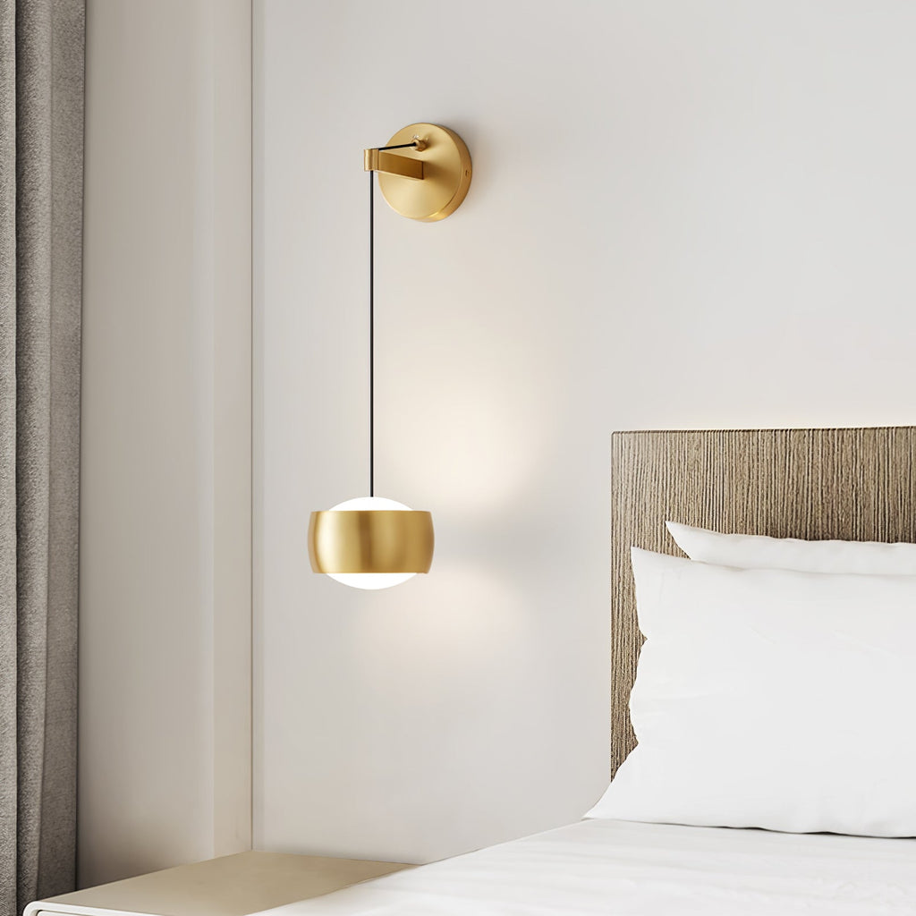 Brass Clérachic wall light glowing beside a bed with white pillows, a wood-slat headboard and a curtain at the left.