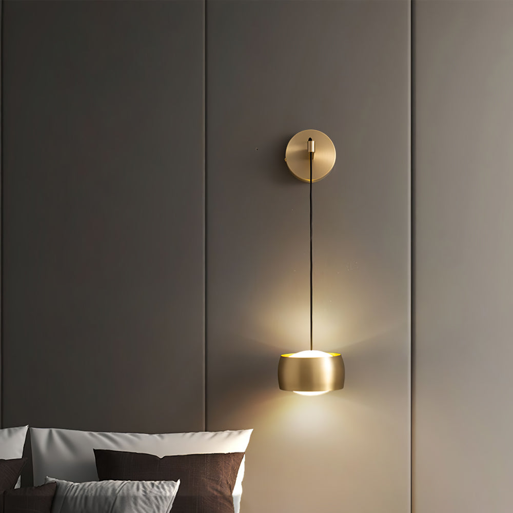 Brass Clérachic wall light throwing light up and down a taupe wall, with brown and grey pillows at the foot of the frame.