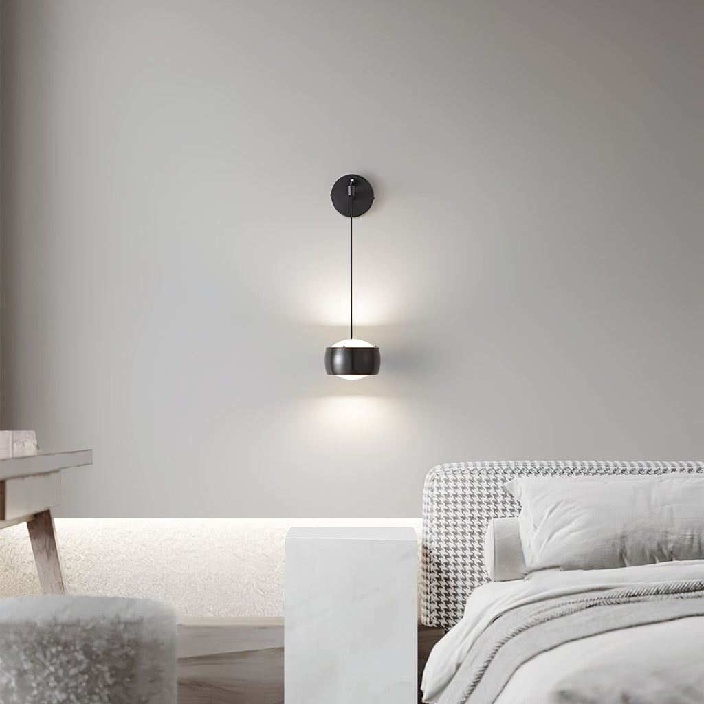 Lit black Clérachic wall light on a pale grey wall, with a houndstooth bench and a marble side table in the room below.