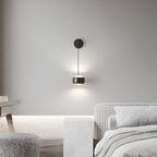 Lit black Clérachic wall light on a pale grey wall, with a houndstooth bench and a marble side table in the room below.