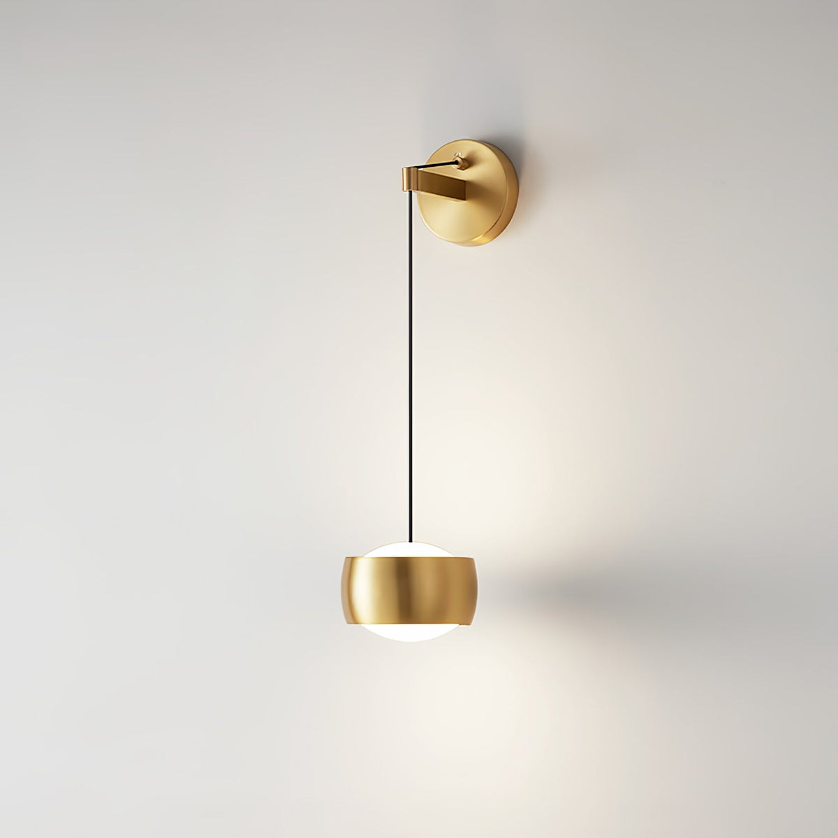 Brass Clérachic wall light on a pale wall, a soft glow from its rounded shade and a long black cable dropping from the backplate.